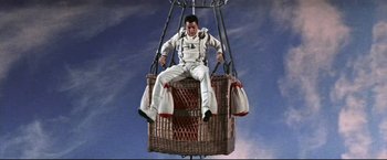 Movie still from “The Great Race” (1965), directed by Blake Edwards – A man sitting on top of a wicker basket; Wide shot, Overhead angle