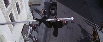 Movie still from “The Great Race” (1965), directed by Blake Edwards – A man hanging from a traffic light on the side of the street; Wide shot, Overhead angle