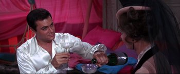 Movie still from “The Great Race” (1965), directed by Blake Edwards – A man pouring champagne into a wine glass while a woman watches; Medium shot, Over the shoulder angle