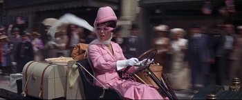 Movie still from “The Great Race” (1965), directed by Blake Edwards – A woman in a pink dress driving a car in the street; Medium shot, Low angle