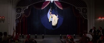 Movie still from “The Great Race” (1965), directed by Blake Edwards – A man and a woman are hanging from a rope in front of an audience; Wide shot, Low angle