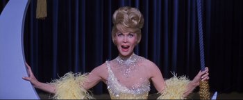 Movie still from “The Great Race” (1965), directed by Blake Edwards – A woman in a yellow and white dress with feathers on her head; Close Up shot, Low angle