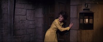 Movie still from “The Great Race” (1965), directed by Blake Edwards – A woman in a yellow coat leaning against a door; Medium shot, High angle