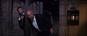 Movie still from “The Great Race” (1965), directed by Blake Edwards – An older man in a suit and tie walking through a doorway; Medium shot, Low angle