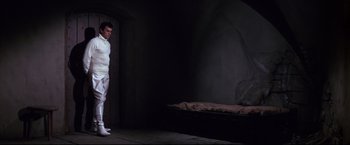 Movie still from “The Great Race” (1965), directed by Blake Edwards – A man standing next to a bed in a dark room; Wide shot, High angle
