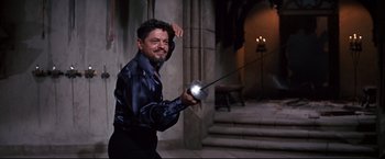 Movie still from “The Great Race” (1965), directed by Blake Edwards – A man holding a sword and a flashlight in front of a stone wall; Medium shot, Over the shoulder angle