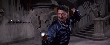Movie still from “The Great Race” (1965), directed by Blake Edwards – A man holding a light in his hand in front of a stone pillar; Medium shot, Low angle