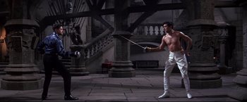 Movie still from “The Great Race” (1965), directed by Blake Edwards – A man in white pants holding a sword in a courtyard; Wide shot, High angle