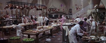 Movie still from “The Great Race” (1965), directed by Blake Edwards – A group of people standing around a table filled with food; Wide shot, High angle