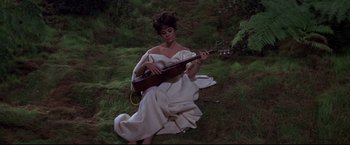 Movie still from “The Great Race” (1965), directed by Blake Edwards – A woman sitting on the ground playing a guitar; Medium shot, High angle