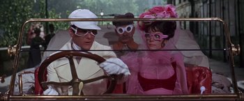 Movie still from “The Great Race” (1965), directed by Blake Edwards – A man driving a car with two women and a man wearing glasses; Medium shot, Over the shoulder angle