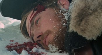 Movie still from “The Great Silence” (1968), directed by Sergio Corbucci – A man with a beard and a bloody headband laying in the snow; Close Up shot, Overhead angle