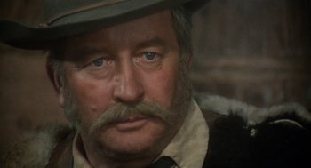 Movie still from “The Great Silence” (1968), directed by Sergio Corbucci – An older man with a mustache and a hat; Close Up shot, Over the shoulder angle