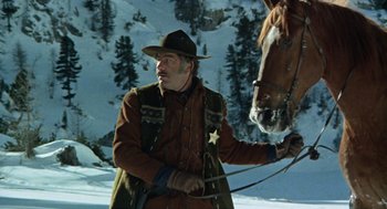Movie still from “The Great Silence” (1968), directed by Sergio Corbucci – A man in a cowboy hat is leading a horse in the snow; Medium shot, Low angle