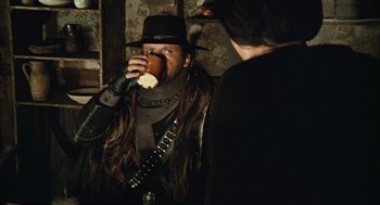 Movie still from “The Great Silence” (1968), directed by Sergio Corbucci – A man with long hair is drinking from a cup; Medium shot, Over the shoulder angle
