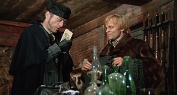 Movie still from “The Great Silence” (1968), directed by Sergio Corbucci – Two men are standing at a table with bottles; Medium shot, Low angle