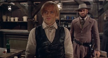 Movie still from “The Great Silence” (1968), directed by Sergio Corbucci – A man wearing a vest and a hat standing next to another man wearing a hat; Medium shot, Low angle