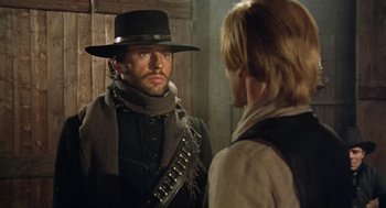 Movie still from “The Great Silence” (1968), directed by Sergio Corbucci – A man wearing a hat and a scarf looking at another man in front of a wooden door; Medium shot, Over the shoulder angle