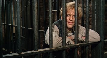 Movie still from “The Great Silence” (1968), directed by Sergio Corbucci – A man leaning up against the bars of a jail cell; Close Up shot, High angle