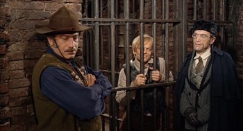 Movie still from “The Great Silence” (1968), directed by Sergio Corbucci – A man in a cowboy hat and vest standing next to another man in a jail cell; Medium shot, High angle