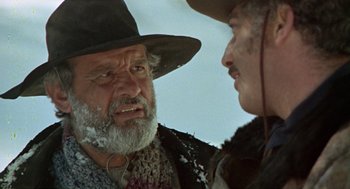 Movie still from “The Great Silence” (1968), directed by Sergio Corbucci – A man with a beard talking to another man in a cowboy hat; Close Up shot, Over the shoulder angle