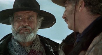 Movie still from “The Great Silence” (1968), directed by Sergio Corbucci – A man with a beard and a cowboy hat talking to another man; Close Up shot, Over the shoulder angle