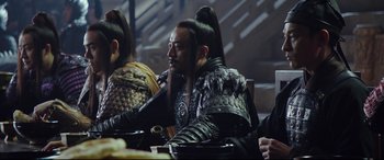 Movie still from “The Great Wall” (2016), directed by Yimou Zhang – A group of people sitting around a table; Medium shot, Over the shoulder angle