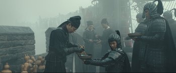 Movie still from “The Great Wall” (2016), directed by Yimou Zhang – A group of people in costume eating food from a bowl; Medium shot, Over the shoulder angle