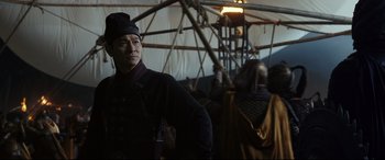 Movie still from “The Great Wall” (2016), directed by Yimou Zhang – A man standing in front of an umbrella in the dark; Medium shot, Over the shoulder angle