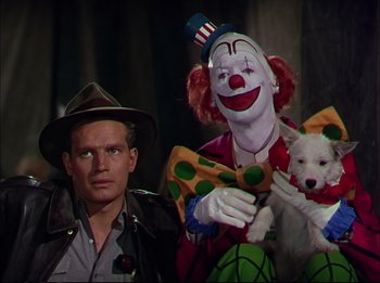 Movie still from “The Greatest Show on Earth” (1952), directed by Cecil B. DeMille – A man sitting next to a clown holding a white dog; Medium shot, Low angle