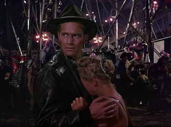 Movie still from “The Greatest Show on Earth” (1952), directed by Cecil B. DeMille – A man and a woman hugging in a crowd of people; Medium shot, Over the shoulder angle