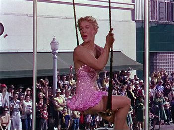 Movie still from “The Greatest Show on Earth” (1952), directed by Cecil B. DeMille – A woman in a pink dress swinging on a rope swing; Wide shot, Low angle