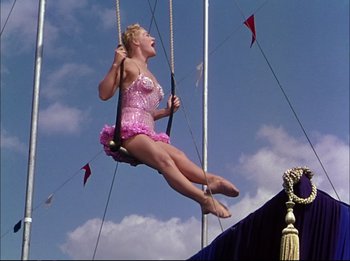 Movie still from “The Greatest Show on Earth” (1952), directed by Cecil B. DeMille – A woman in a pink bathing suit swinging on a rope; Wide shot, Low angle