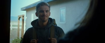 Movie still from “The Guest” (2014), directed by Adam Wingard – A man with a backpack smiles for the camera; Close Up shot, Over the shoulder angle