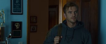 Movie still from “The Guest” (2014), directed by Adam Wingard – A young man holding a backpack in a dark room; Close Up shot, Over the shoulder angle