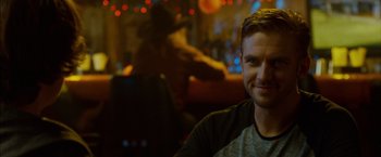 Movie still from “The Guest” (2014), directed by Adam Wingard – A man sitting at a table in front of lights; Close Up shot, Over the shoulder angle