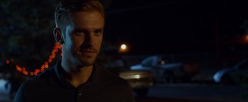 Movie still from “The Guest” (2014), directed by Adam Wingard – A person wearing a black shirt near a car; Close Up shot, Over the shoulder angle