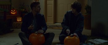 Movie still from “The Guest” (2014), directed by Adam Wingard – Two men sitting next to each other holding pumpkins; Medium shot, Over the shoulder angle