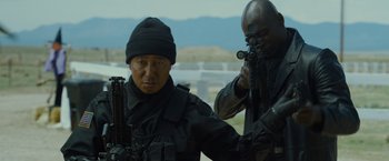 Movie still from “The Guest” (2014), directed by Adam Wingard – A man in black jacket holding a gun next to another man in black jacket; Medium shot, Over the shoulder angle