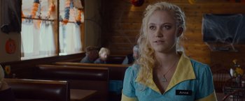 Movie still from “The Guest” (2014), directed by Adam Wingard – A woman sitting at a table in front of a group of people; Close Up shot, Over the shoulder angle