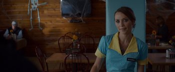 Movie still from “The Guest” (2014), directed by Adam Wingard – A woman standing in front of a wooden table and chairs; Medium shot, Over the shoulder angle