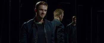 Movie still from “The Guest” (2014), directed by Adam Wingard – A man standing in front of another man in a dark room; Medium shot, Over the shoulder angle