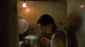 Movie still from “The Hand” (2004), directed by Kar-Wai Wong – A man is cooking in a kitchen under a lamp; Medium shot, Low angle