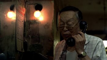 Movie still from “The Hand” (2004), directed by Kar-Wai Wong – An older man talking on a phone in front of a light; Close Up shot, High angle