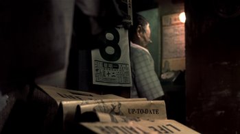Movie still from “The Hand” (2004), directed by Kar-Wai Wong – A man standing in front of a stack of newspapers; Extreme Close Up shot, Low angle