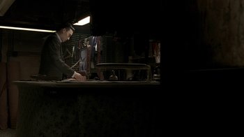 Movie still from “The Hand” (2004), directed by Kar-Wai Wong – A man standing in front of an ironing board in a dark room; Medium shot, High angle