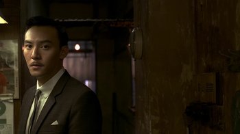 Movie still from “The Hand” (2004), directed by Kar-Wai Wong – A man wearing a suit and tie standing next to a wall; Close Up shot, Over the shoulder angle