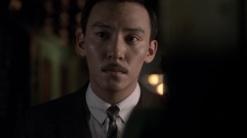 Movie still from “The Hand” (2004), directed by Kar-Wai Wong – A man in a suit and tie looking at the camera; Close Up shot, Over the shoulder angle