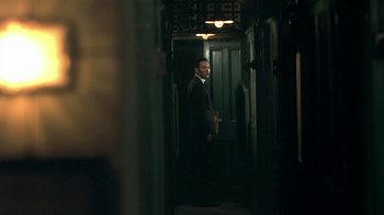 Movie still from “The Hand” (2004), directed by Kar-Wai Wong – A man in a suit standing in a dark hallway; Medium shot, Over the shoulder angle