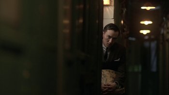 Movie still from “The Hand” (2004), directed by Kar-Wai Wong – A man wearing a suit and tie holding a book; Medium shot, Low angle